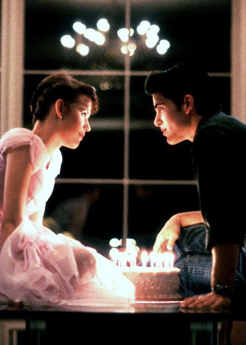 a man and woman sitting next to each other in front of a cake with candles on it