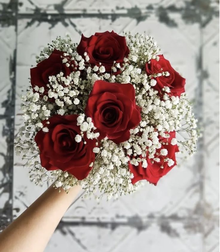 a bouquet of red roses and baby's breath is being held by a hand