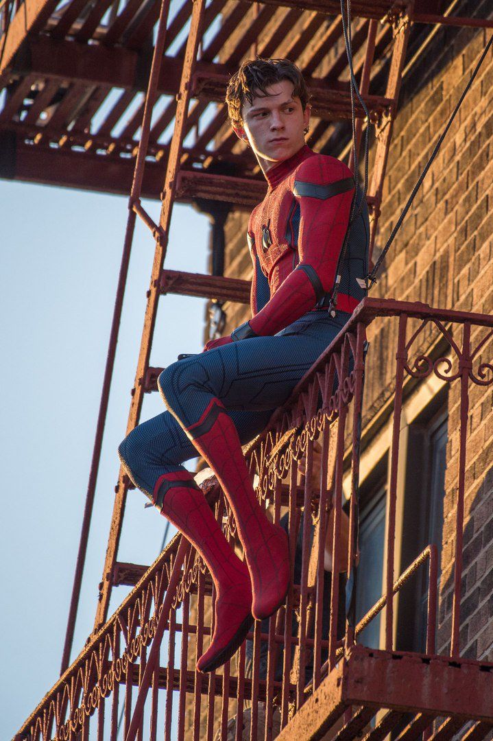 a young man dressed as spider - man sitting on the top of a fire escape