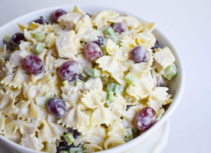 a white bowl filled with pasta salad and grapes