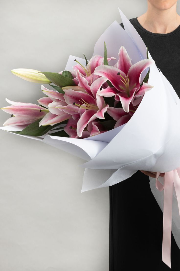 a woman holding a bouquet of pink flowers in her left hand and wearing a black shirt