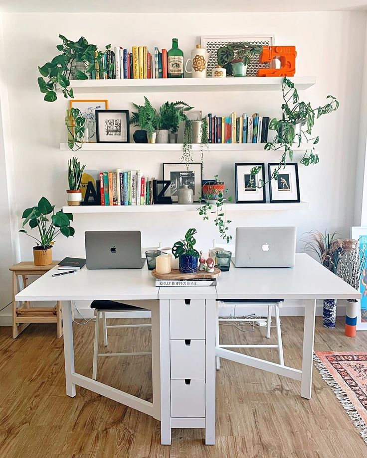 a white desk with two laptops on it and some bookshelves behind it