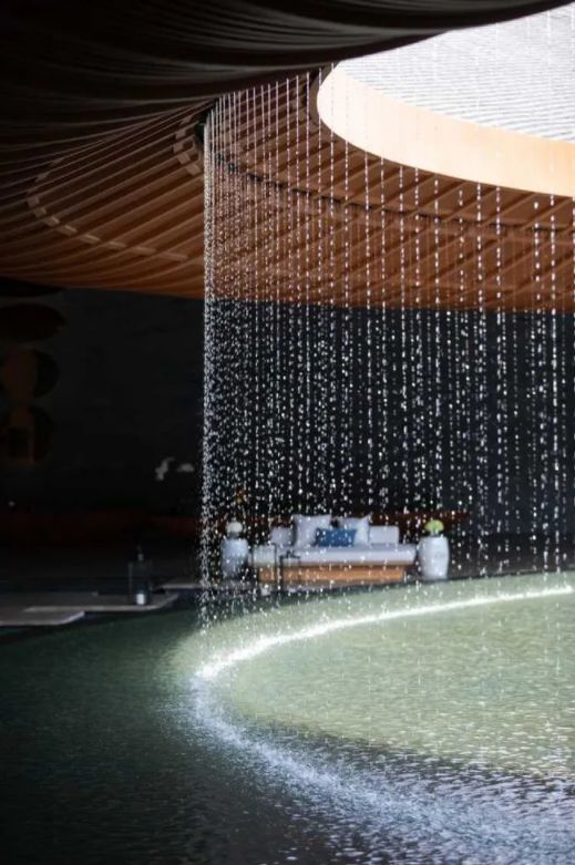 a fountain with water running down it and some couches in the background, under an awning