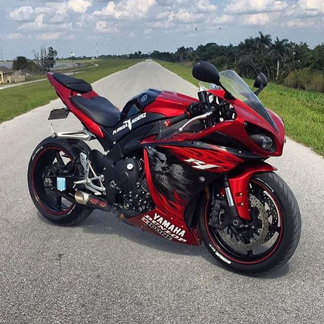 a red and black motorcycle parked on the side of a road in front of some grass