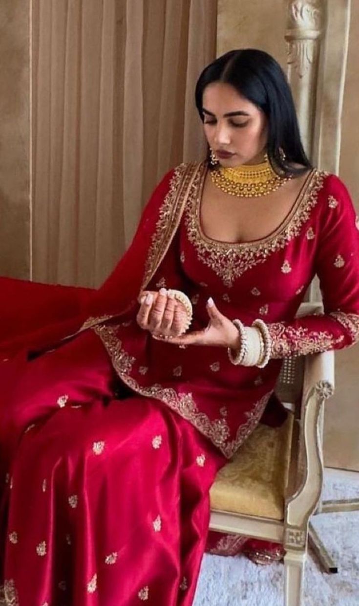 a woman sitting in a chair wearing a red dress with gold jewelry on her neck