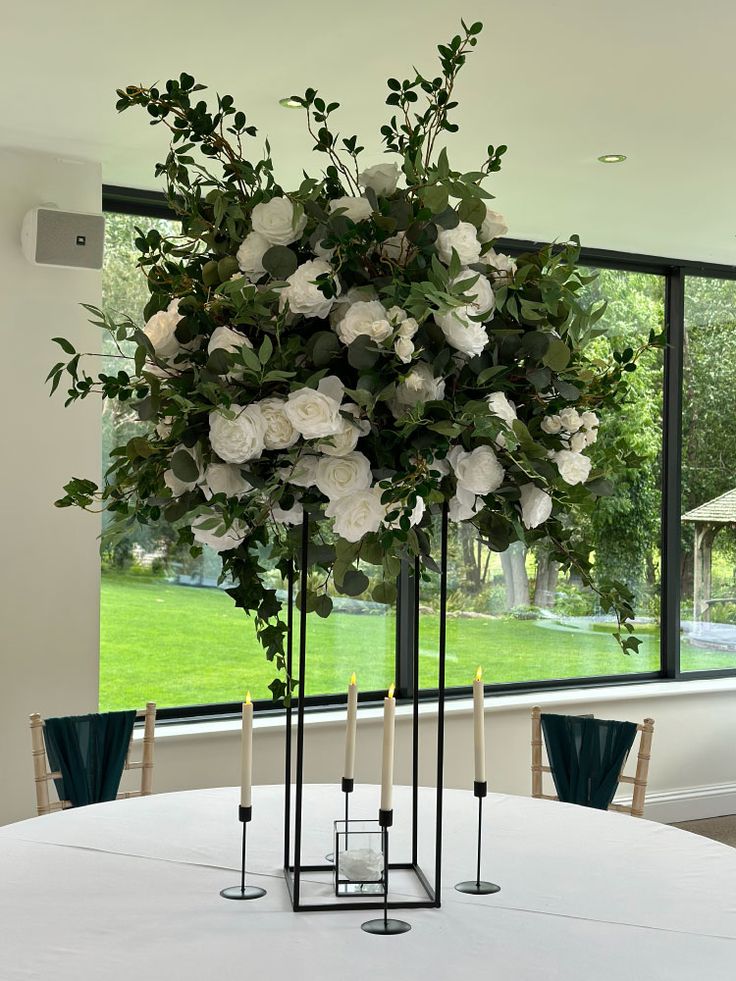 a table with candles and flowers on it in front of a large window that looks out onto a green lawn