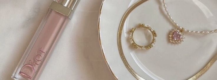 a white plate topped with a necklace next to a pink lip balm bottle on top of a table