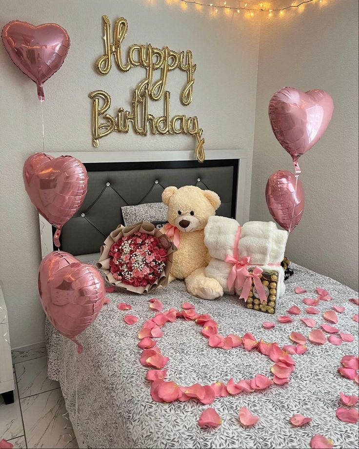 a teddy bear sitting on top of a bed surrounded by balloons