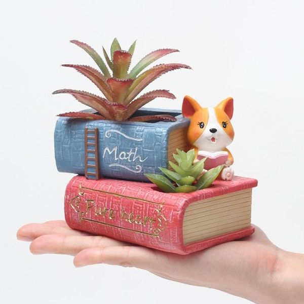 a small dog figurine sitting on top of a stack of books next to a succulent plant