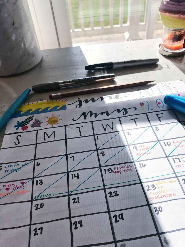 a calendar with writing on it next to some markers and pencils in front of a window