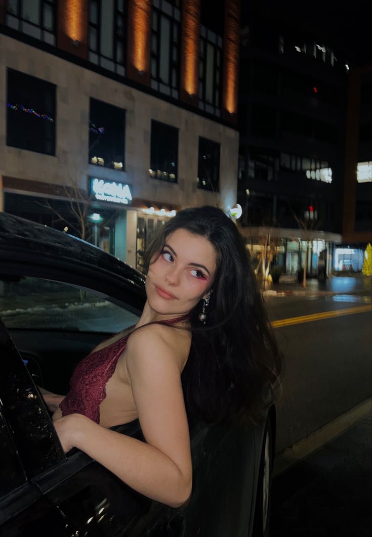 a woman in a red dress leaning out the window of a black car at night