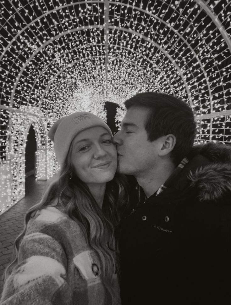 a man and woman are kissing in front of christmas lights at the park, black and white photo