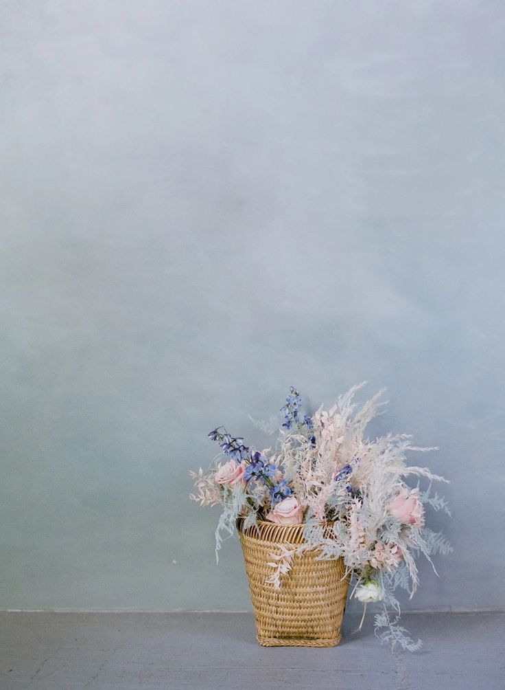 a basket filled with lots of flowers sitting on top of a wooden floor next to a wall