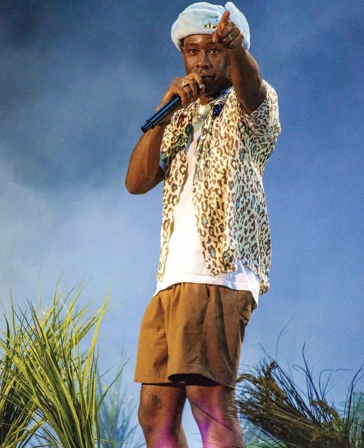 a man standing on top of a stage holding a microphone in his right hand and wearing shorts