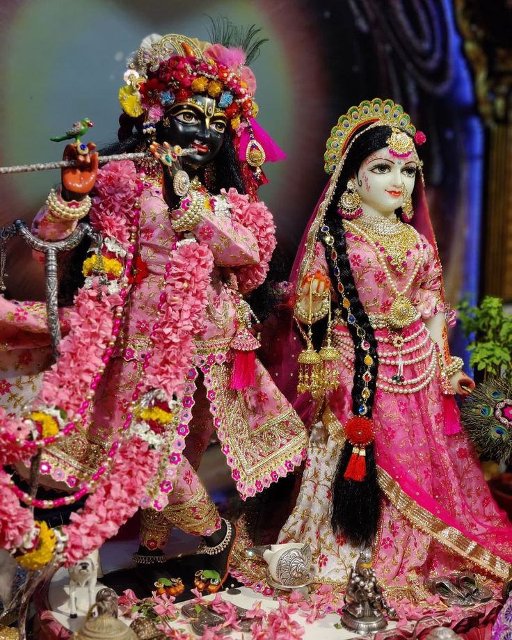 a statue of two people dressed in pink and gold with flowers on the ground next to them