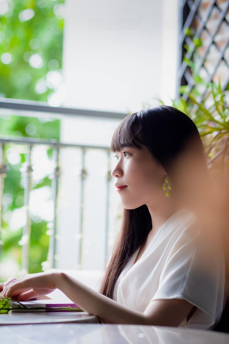 a woman sitting at a table with a laptop in front of her, looking off into the distance