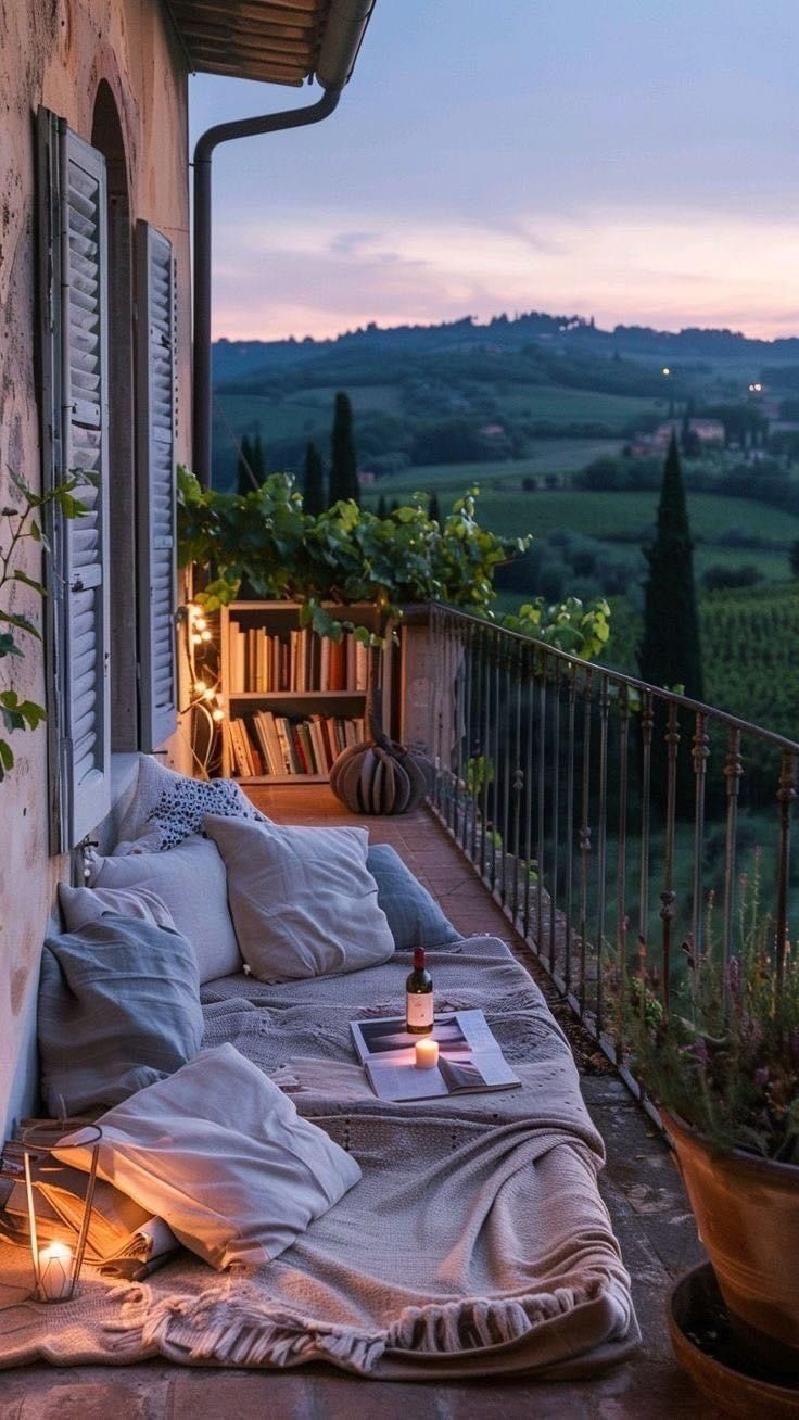 an outdoor bed with pillows and blankets on top of it next to a balcony overlooking the countryside