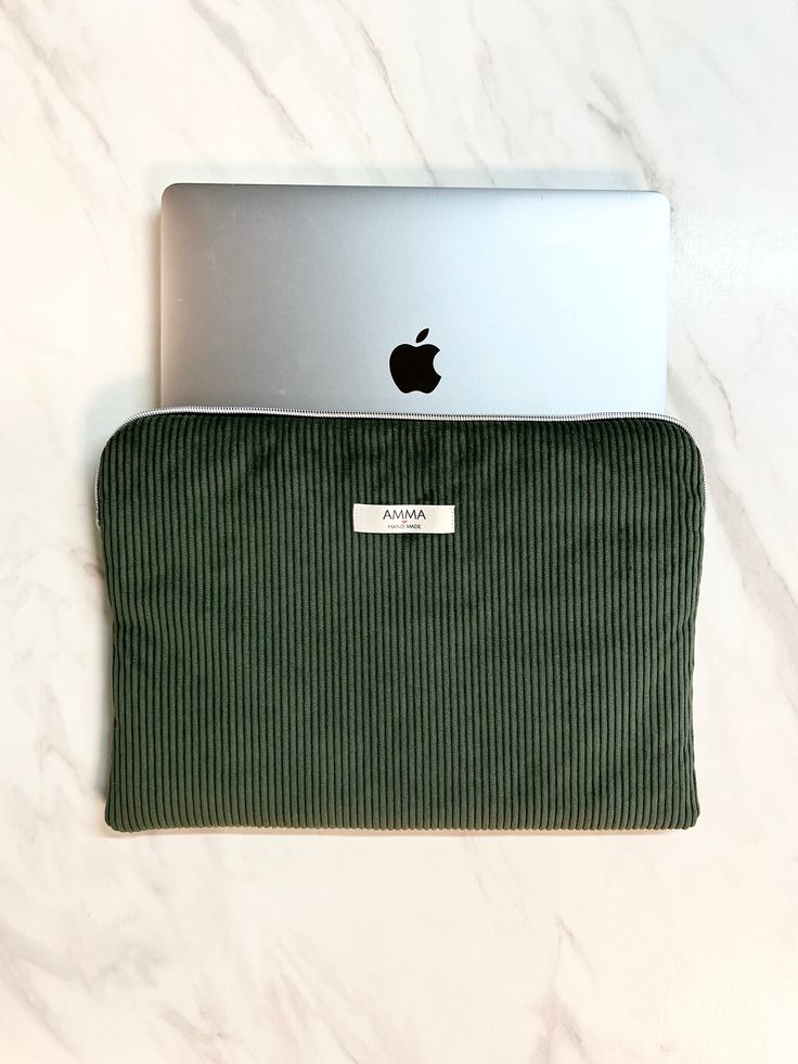 an apple laptop computer sitting on top of a green corded case next to a white marble counter