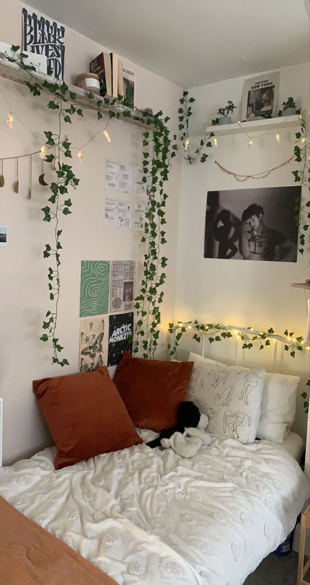 an unmade bed with white sheets and red pillows in a bedroom decorated with ivy