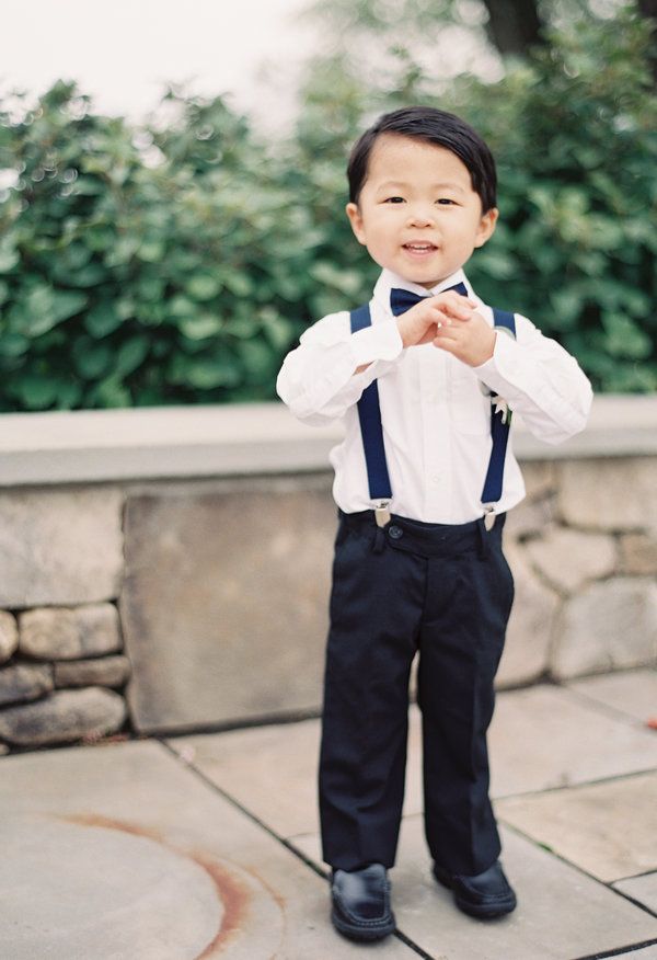 a little boy that is standing up wearing a bow tie and suspenders with his hands in his pockets