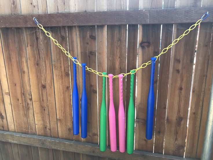 several colorful plastic toothbrushes hanging from a chain on a wooden fence in the backyard