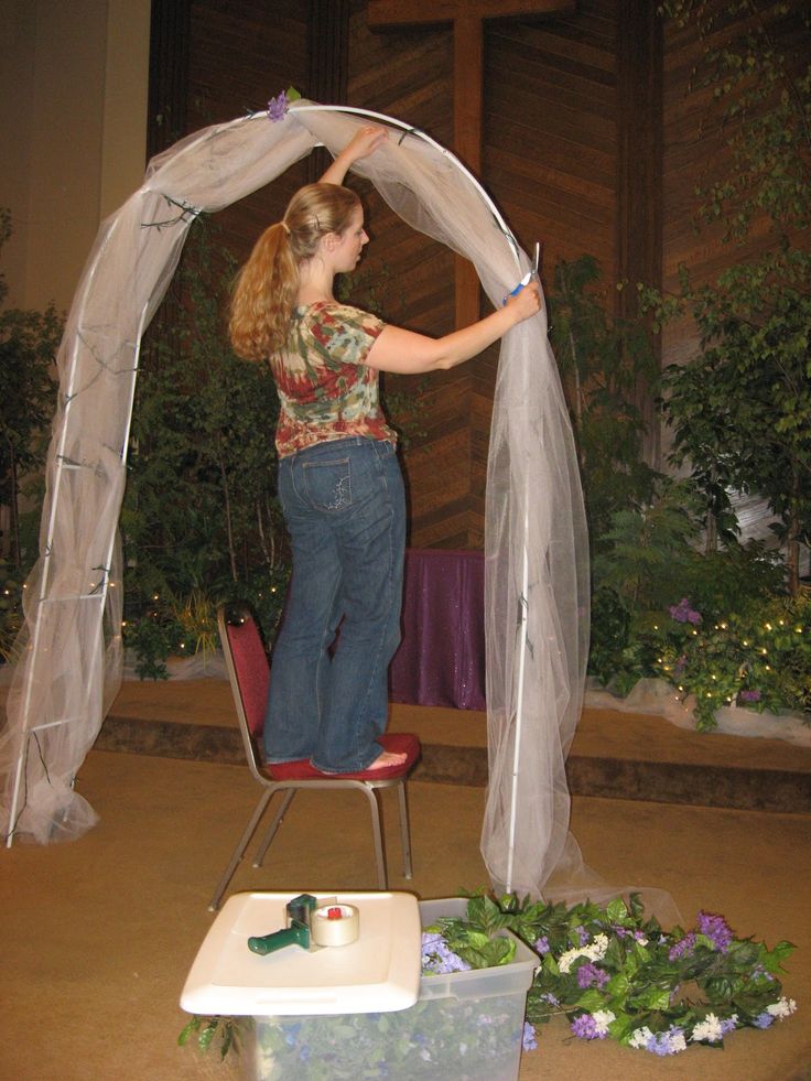 a woman standing on top of a chair in front of a white net covered arch