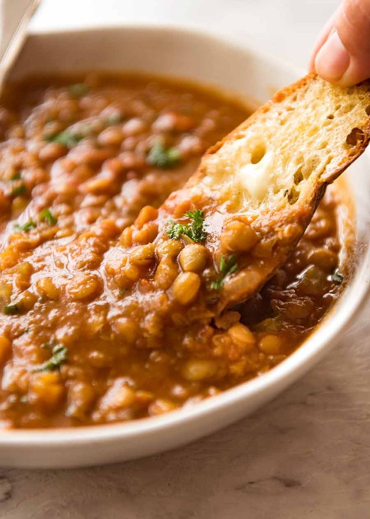 a hand holding a piece of bread over a bowl of beans