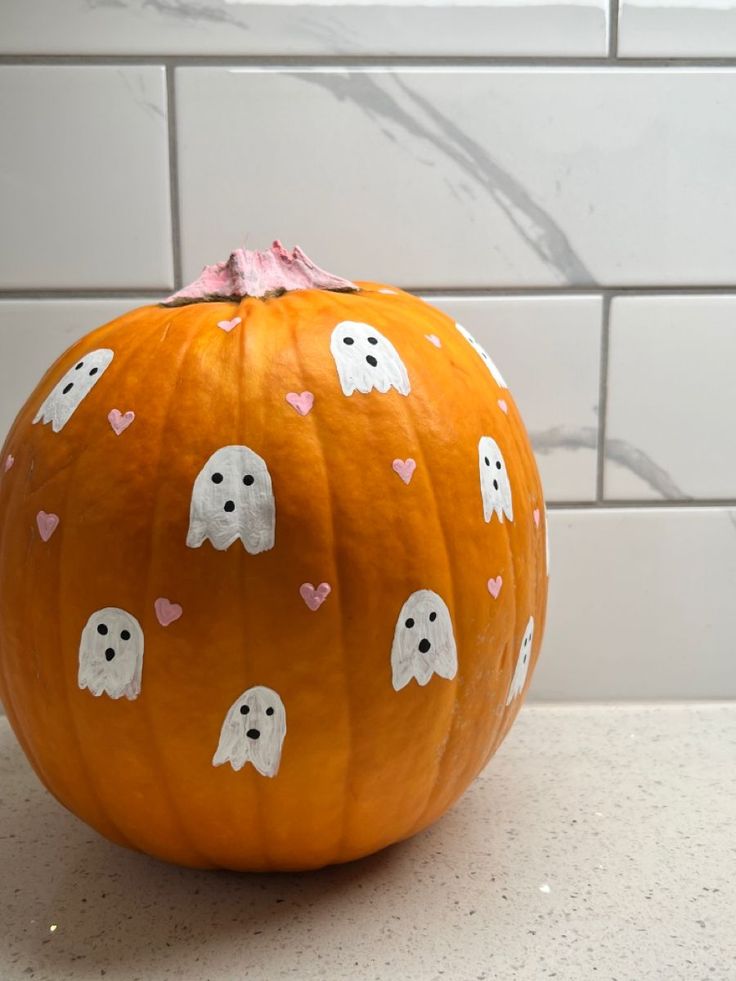 an orange pumpkin decorated with ghost faces and pink hearts on it's face, sitting on a counter