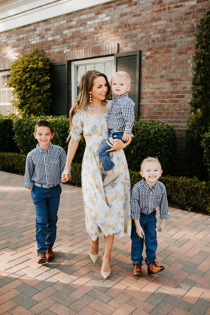 a woman and two boys walking down the street with their mother holding her son's hand