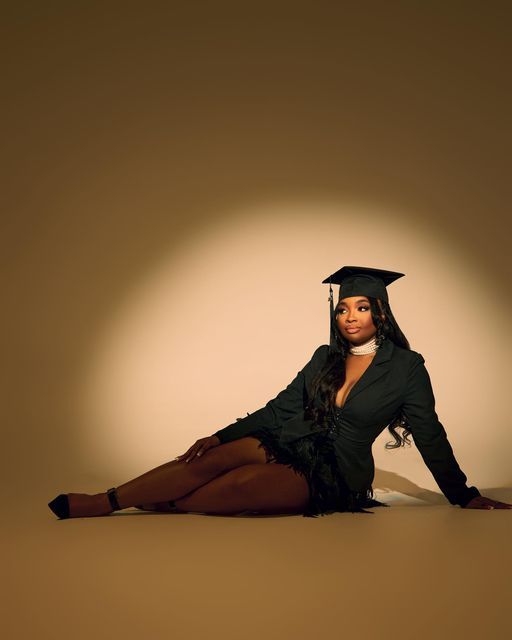 a woman in a graduation cap and gown sitting on the floor with her legs crossed