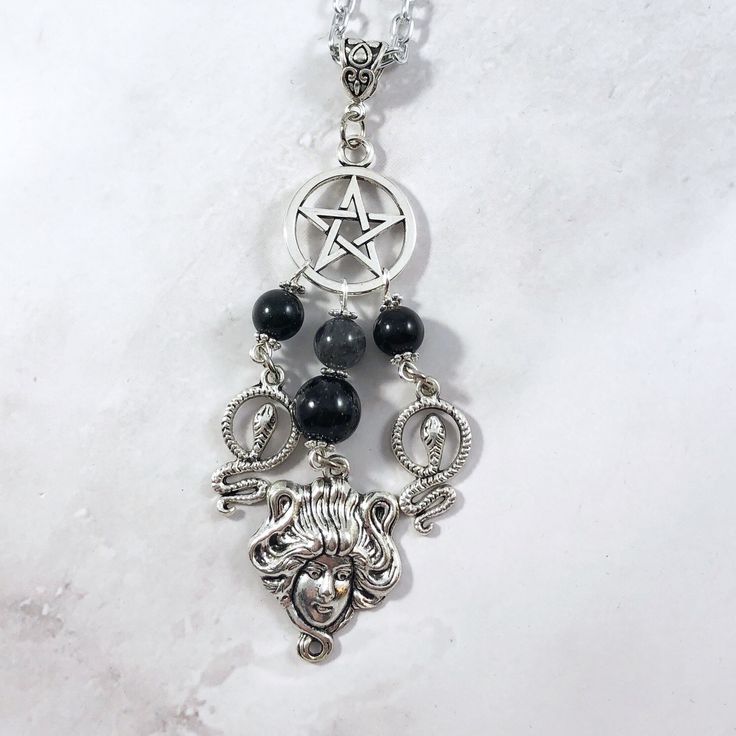 This Medusa pendant necklace is the perfect way to express your affinity for the Greek myths in subtle way. Pendant is made with four charms: Pentacle Medusa Head 2 snake charms 3 tourmaline beads and one labradorite bead also make up the pendant. Available in a variety of lengths. Chain is stainless steel, charms are zinc alloy and beads are natural gemstone. All materials are lead and nickel free. Comes in a jewelry box so it's ready to be given as a gift. Have a idea for a custom order? I'd l Mystical Silver Gemstone Bead Necklace, Mystical Silver Necklace With Gemstone Beads, Spiritual Silver Charm Necklaces With Gemstone Beads, Spiritual Black Dangle Necklaces, Symbolic Black Necklace With Moon Charm, Spiritual Black Necklaces With Charms, Spiritual Silver Onyx Beaded Necklaces, Medusa Necklace, Medusa Pendant