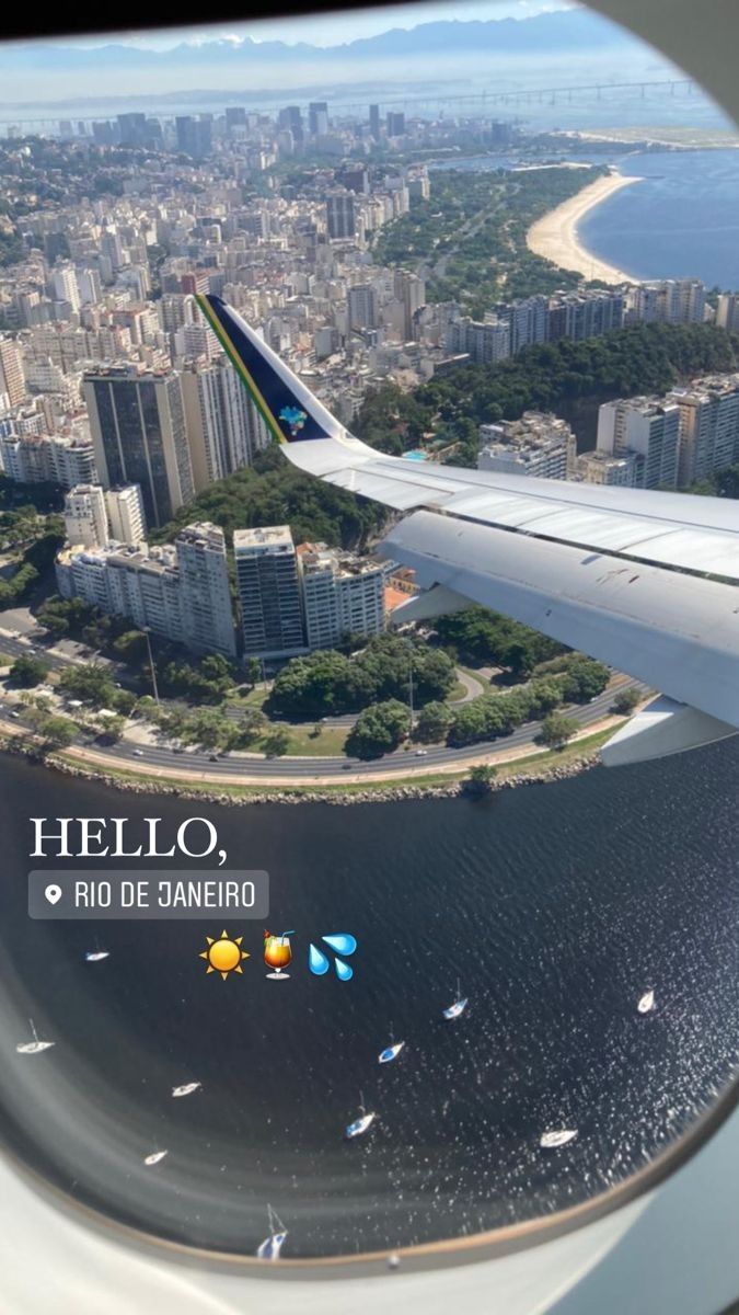 an airplane wing flying over a city next to the ocean with buildings in the background