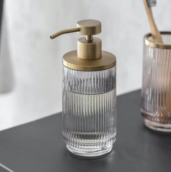 two glass containers with toothbrushes and soap dispenser sitting on a counter