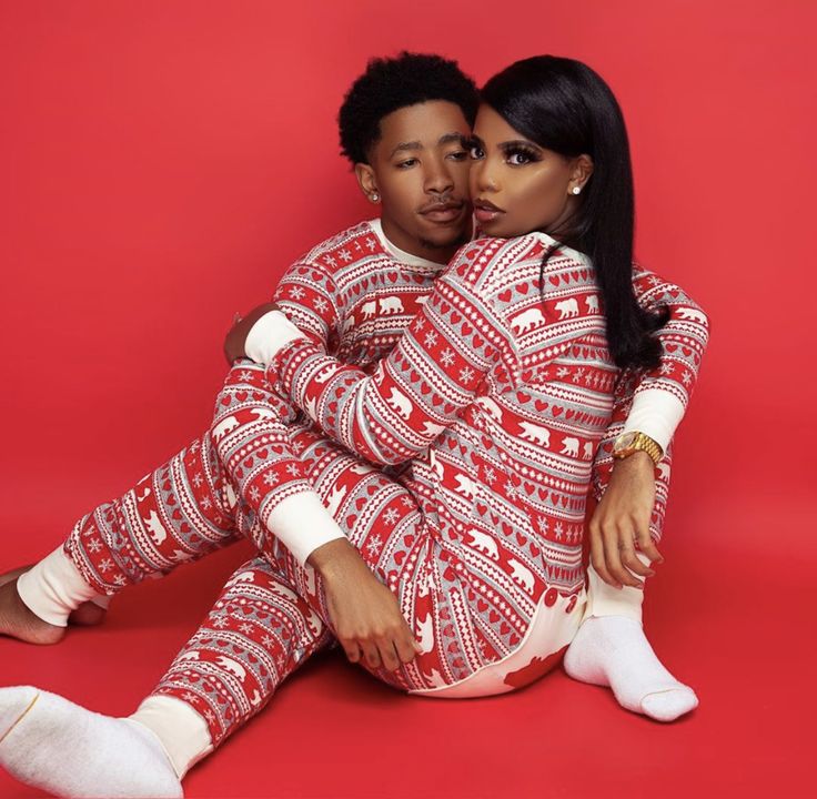 a man and woman sitting on the floor in matching pajamas, posing for a photo