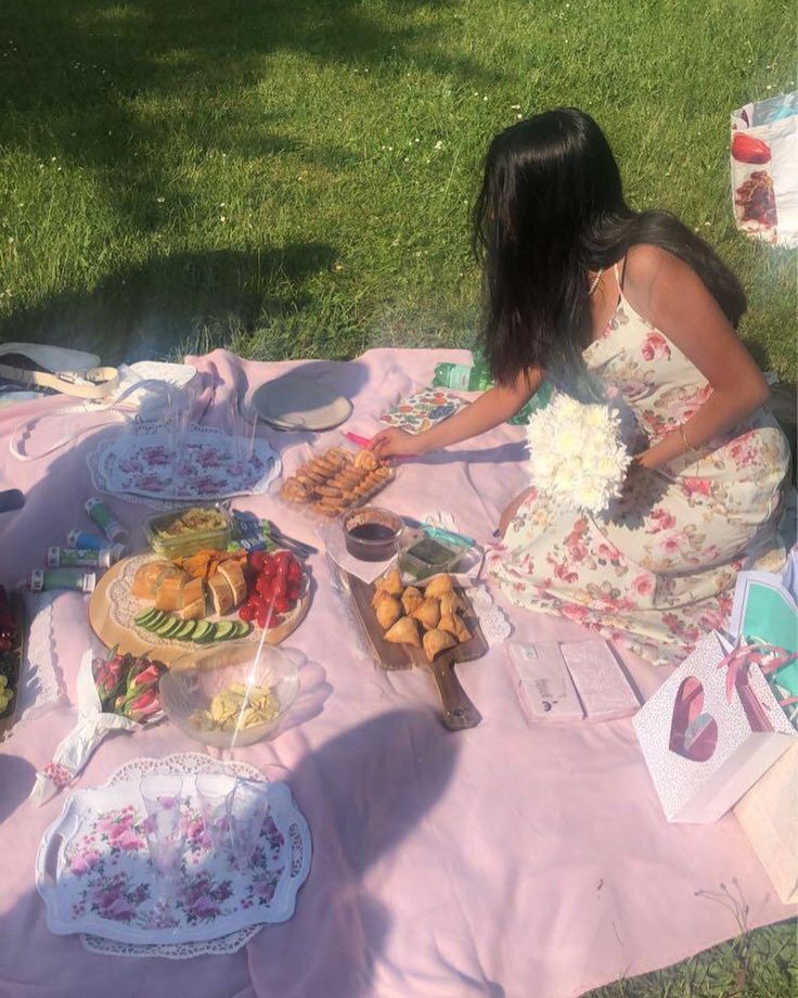 a woman sitting at a picnic table with food on the ground and plates in front of her