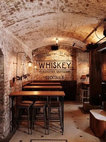 the inside of a brick building with tables and stools in front of an old sign