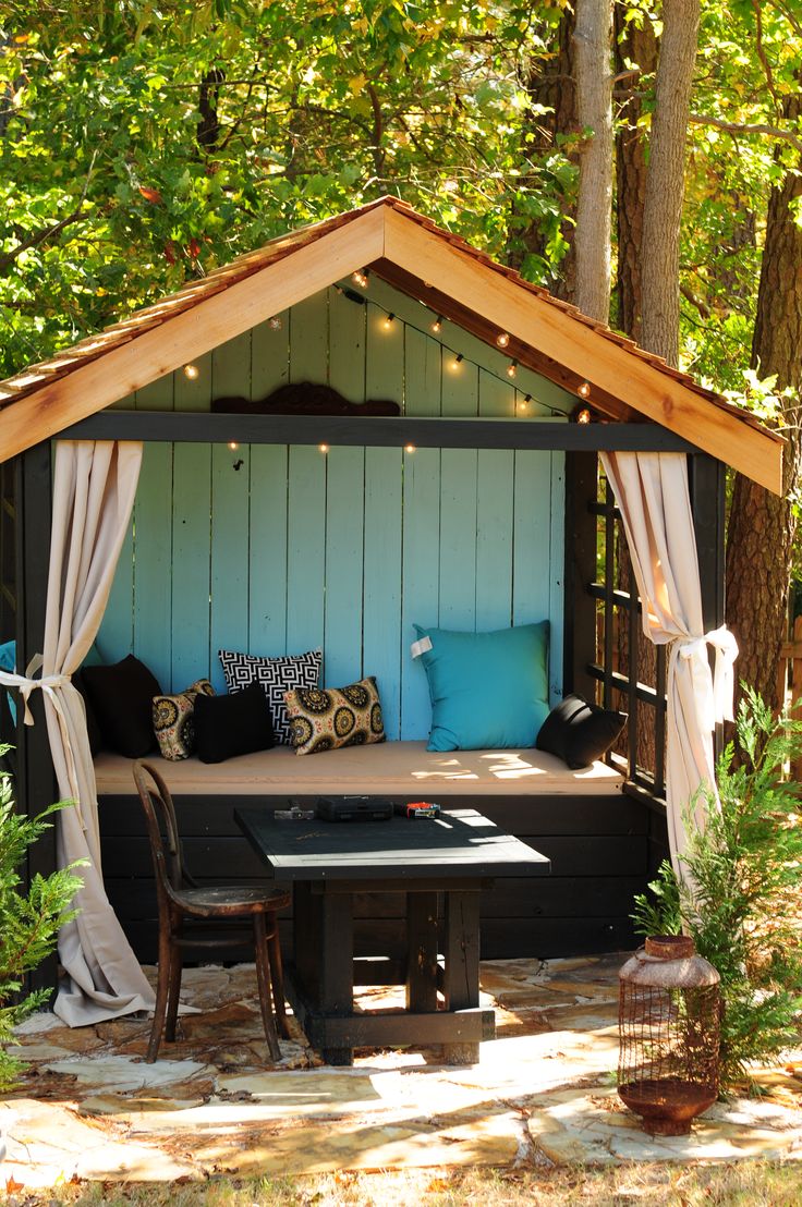 a gazebo with curtains and lights on it in the middle of a wooded area