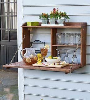 an outdoor shelf with drinks and glasses on it, hanging from the side of a house