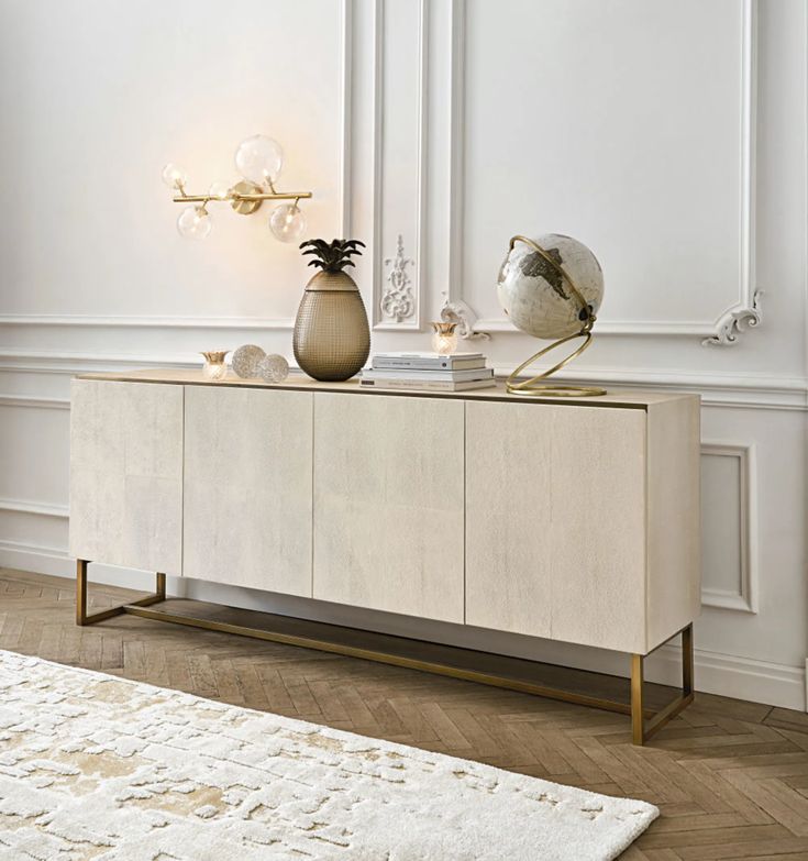 a white and gold sideboard with two pineapples on top, next to a rug