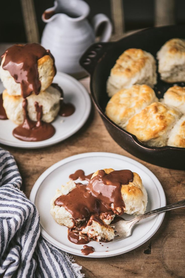 two plates with biscuits covered in chocolate sauce next to a cast iron skillet filled with biscuits