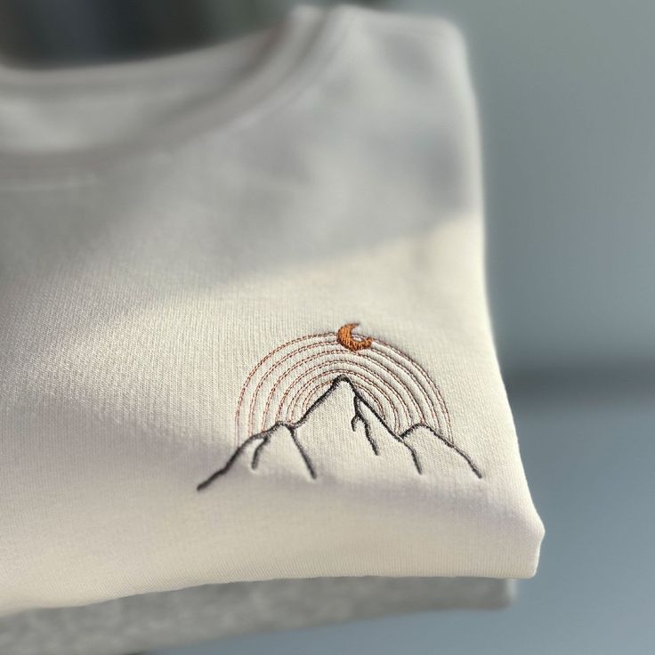 a white t - shirt with an embroidered rainbow on the front and mountains in the back