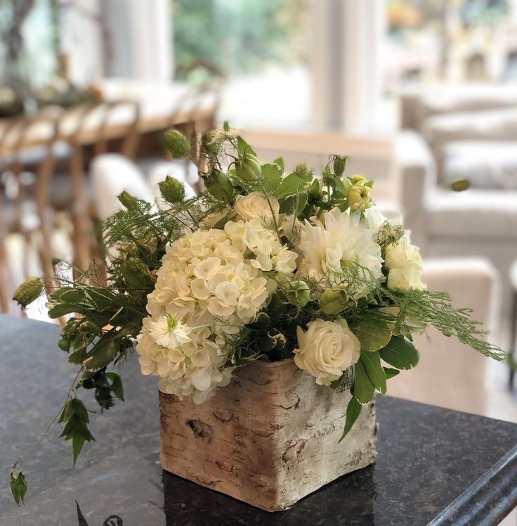 a wooden block with white flowers and greenery in it sitting on a counter top