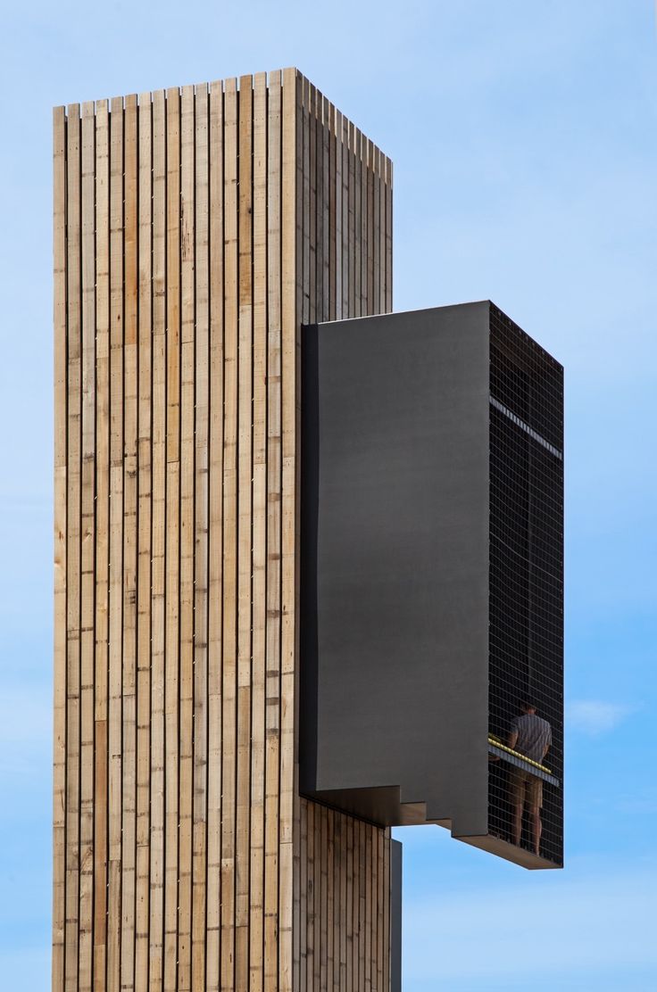 a tall wooden building with people standing on the balcony and looking at something in the distance