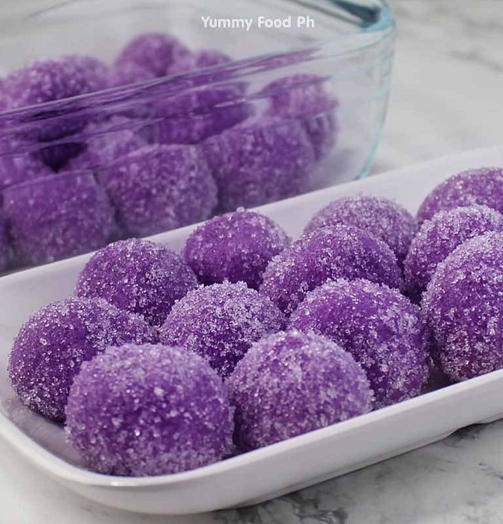 purple sugar balls in a white dish on a marble counter next to a glass container