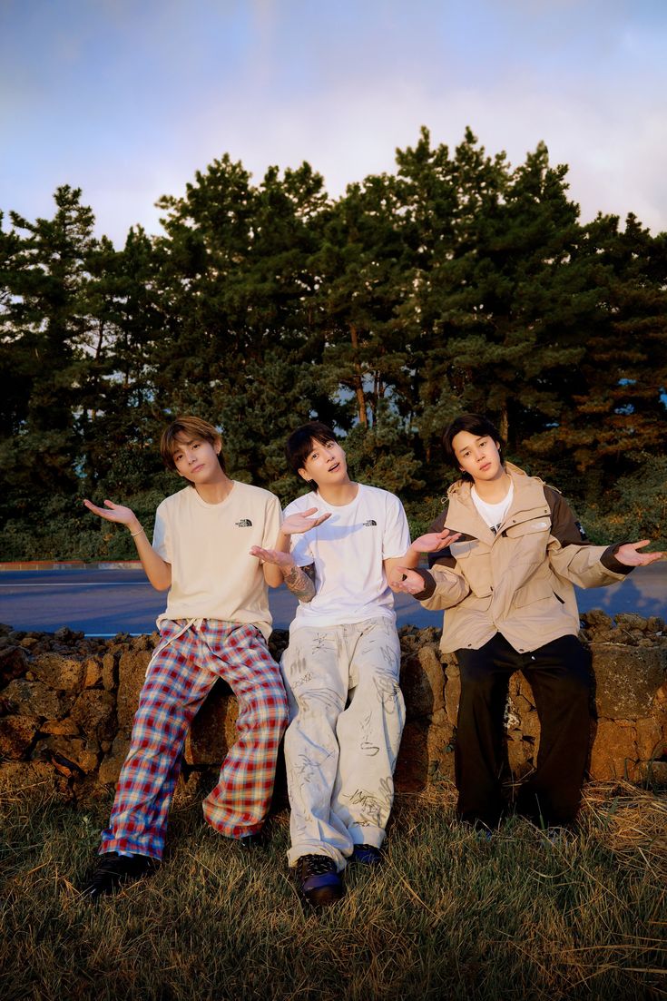 three young men posing for a photo in front of some trees and grass with their arms outstretched