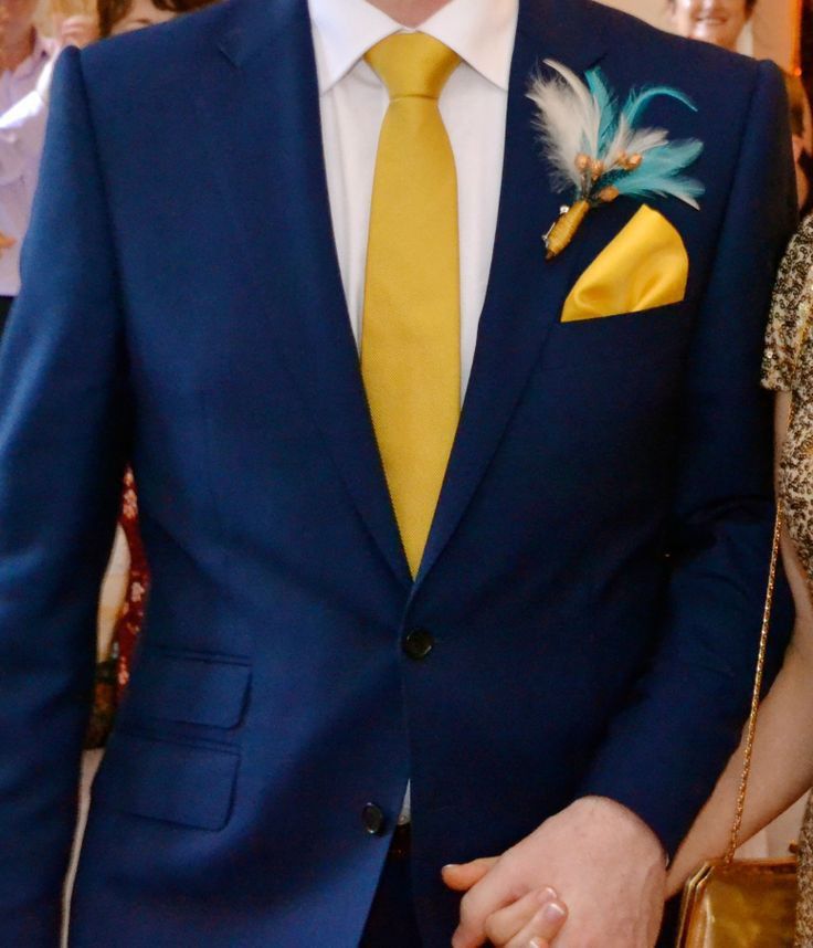 a man in a blue suit and yellow tie standing next to a woman wearing a gold dress