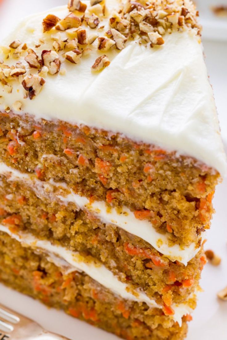 a slice of carrot cake with white frosting on a plate next to a fork