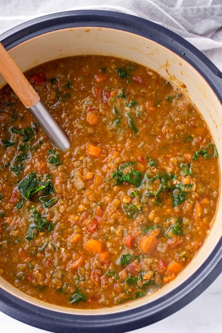 a pot filled with soup on top of a white cloth covered table next to a wooden spoon