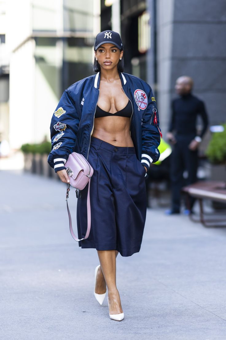 a woman in a crop top and skirt walking down the street with her handbag