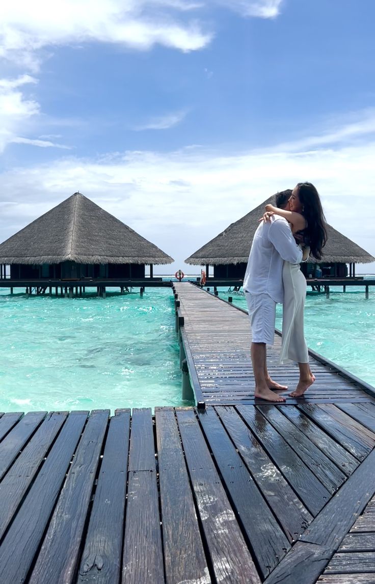 a woman standing on a dock in front of some water and thatched huts over looking the ocean